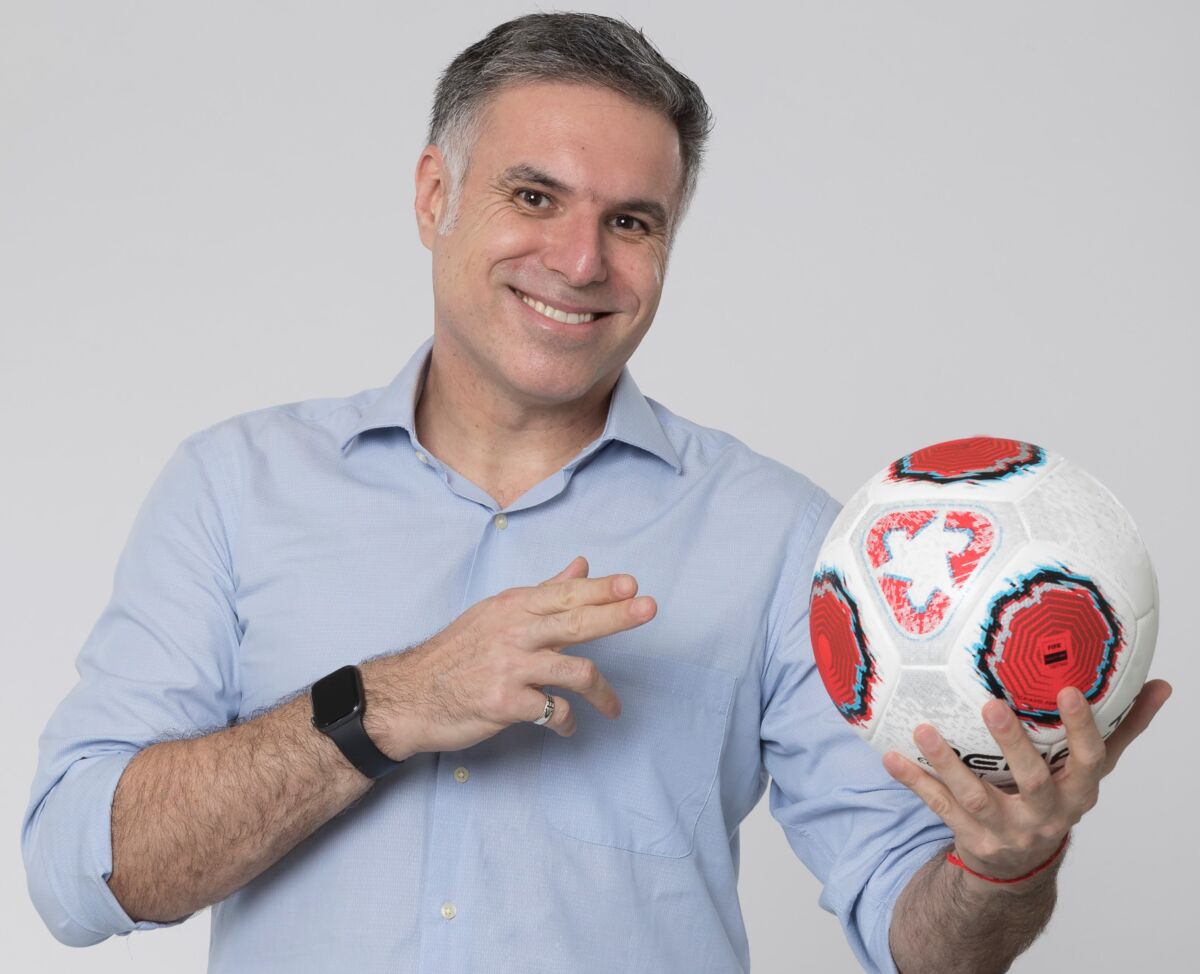 Narrador Marco de Varga posando para foto de divulgação segurando uma bola de futebol com a mão esquerda