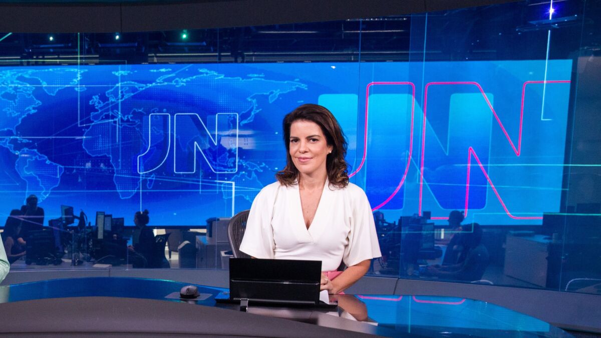 Mariana Gross de blusa branca sentada na bancada do Jornal Nacional 