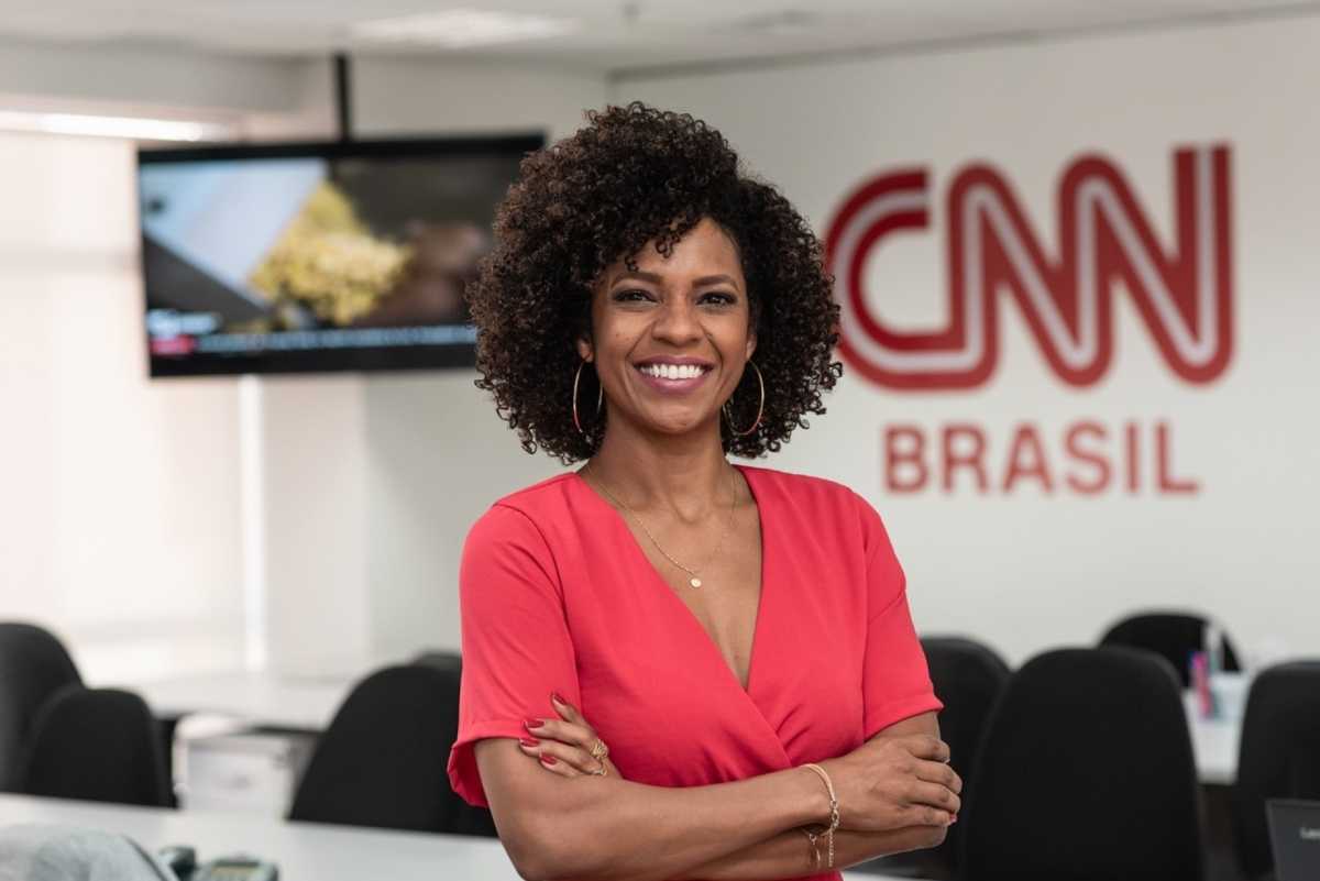 Foto da jornalista Luciana Barreto posando em frente ao logo da CNN