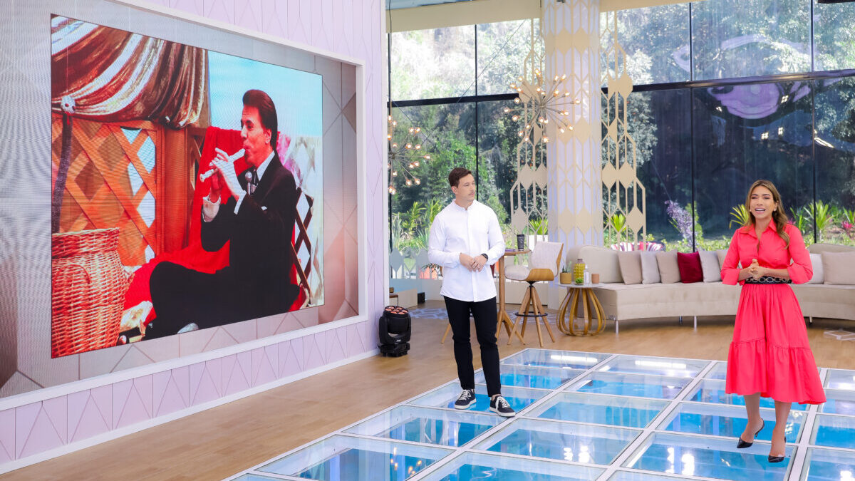 Silvio Santos ao fundo em uma imagem de arquivo no telão, Gabriel Cartolano e Patrícia Abravanel à frente, na edição de 19 de agosto do Vem Pra Cá, nos estúdios do SBT