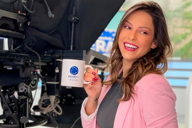 Nikole Lima segura caneca com o logo da Record TV Brasília, onde apresenta o Balanço Geral Manhã