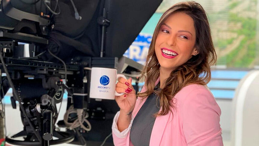 Nikole Lima segura caneca com o logo da Record TV Brasília, onde apresenta o Balanço Geral Manhã