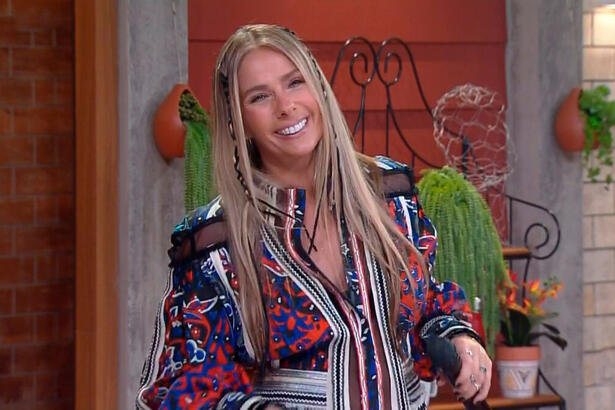 Adriane Galisteu sorrir segurando o microfone enquanto apresenta A Fazenda 13, ao vivo