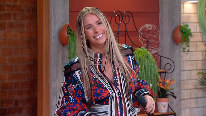 Adriane Galisteu sorrir segurando o microfone enquanto apresenta A Fazenda 13, ao vivo
