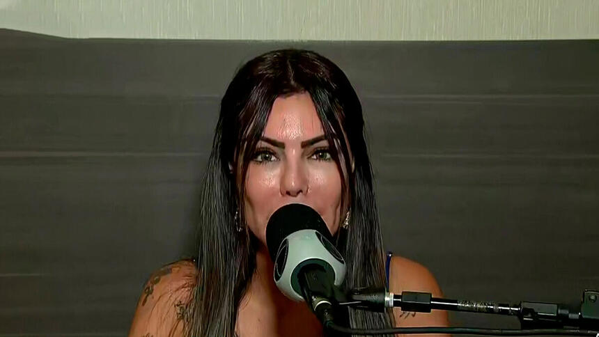 Liziane Gutierrez falando no microfone da Record TV na coletiva de A Fazenda 13