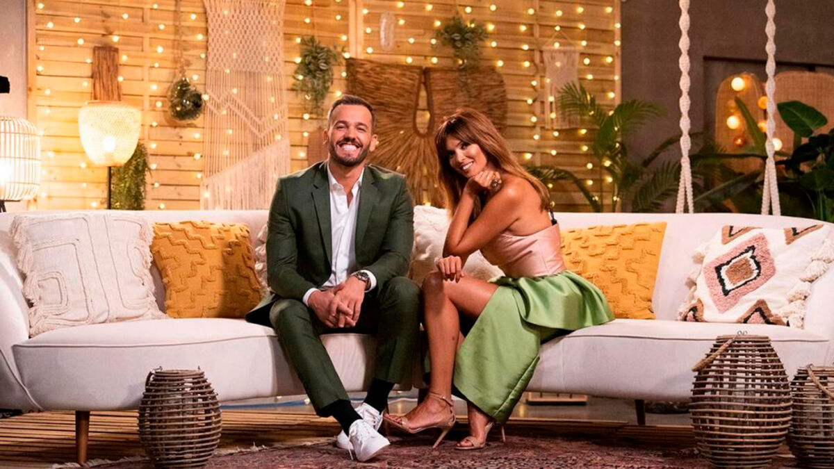 Apresentadora Maria Cerqueira Gomes senta ao lado do apresentador Pedro Teixeira sentados no sofá do cenário do programa O Amor Acontece
