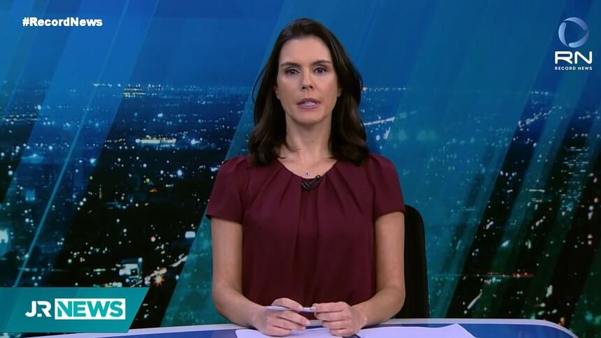 Camila Busnello sentada na bancada nos estúdios do Jornal da Record News