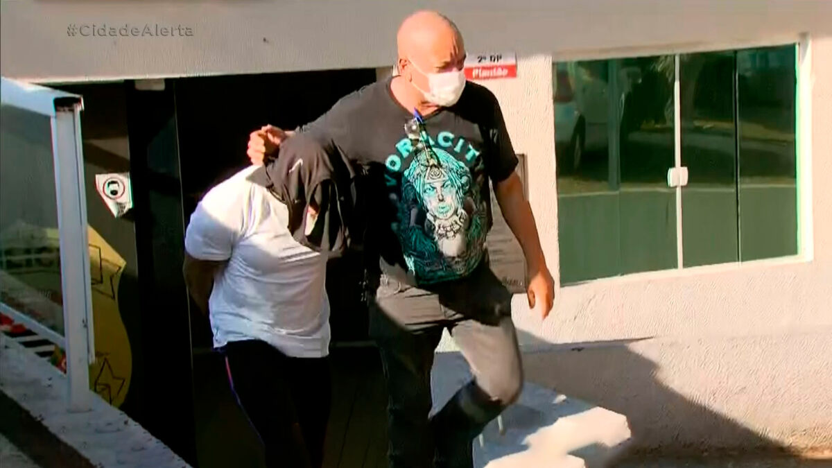 André Luís dos Santos com uma camisa cobrindo o rosto é levado por um policial ao ser preso
