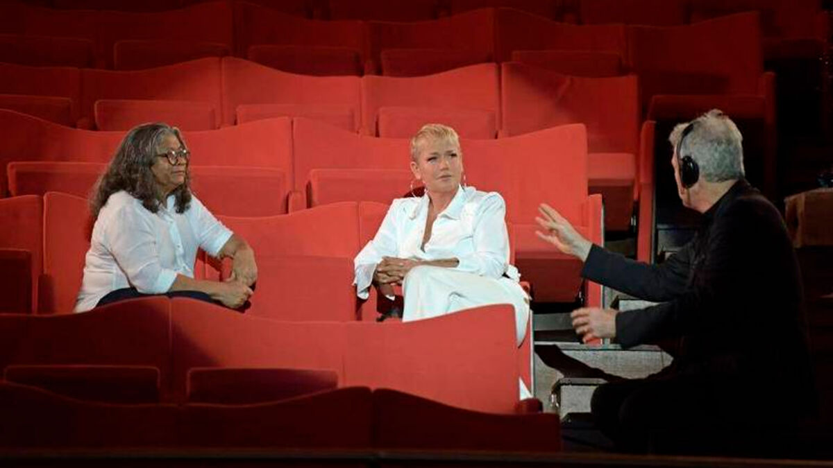 Marlene Mattos sentada ao lado de Xuxa observa as instruções de Pedro Bial