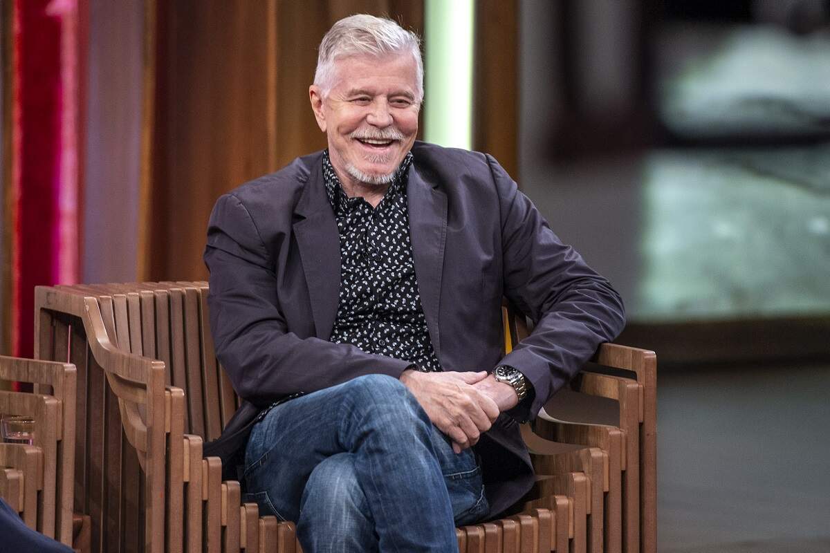 Miguel Falabella de calça jeans e blazer preto sentado em uma cadeira