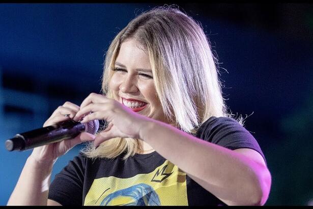 Marília Mendonça durante um show fazendo um coração com as mãos