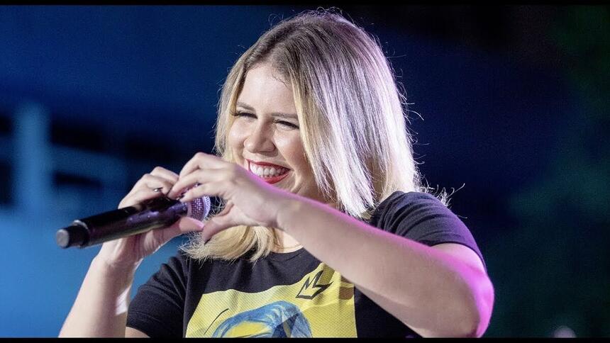 Marília Mendonça durante um show fazendo um coração com as mãos