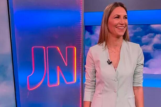 Anne Lottermann sorrir em frente ao logo do Jornal Nacional