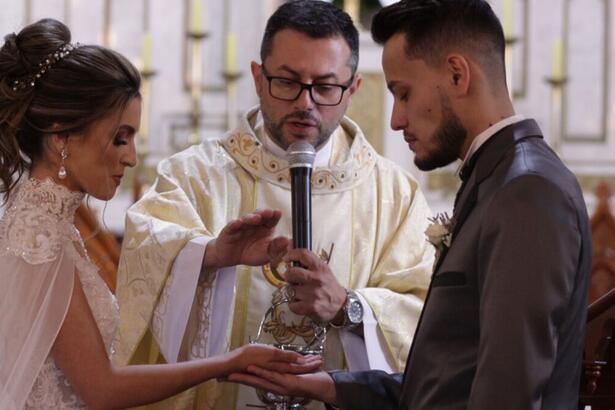 Casal recebendo a benção do padre durante um casamento, em trecho do reprodução do arquivo A