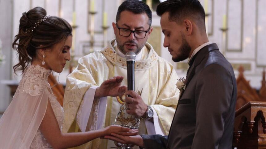 Casal recebendo a benção do padre durante um casamento, em trecho do reprodução do arquivo A