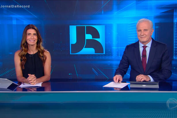 Janine Borba ao lado de Celo Freitas, ambos estão sorrindo, após se despedirem do público no final do Jornal da Record desta terça-feira, 28 de dezembro de 2021