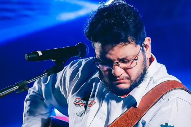 Cantor Maurílio se apresentando durante um show tocando um violão