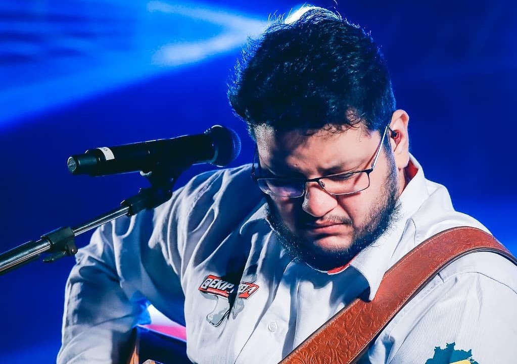 Cantor Maurílio se apresentando durante um show tocando um violão