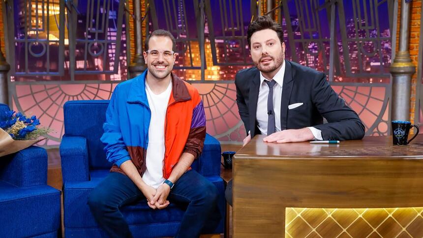 Paulo Mathias sentado na poltrona azul ao lado de Danilo Gentili nos estúdios do The Noite