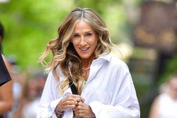 Sarah Jessica Parker posa para foto no meio da rua com casaco branco