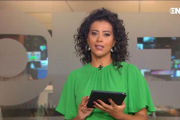 Aline Midlej de blusa verde e tablet na mão nos estúdios do Jornal da Dez