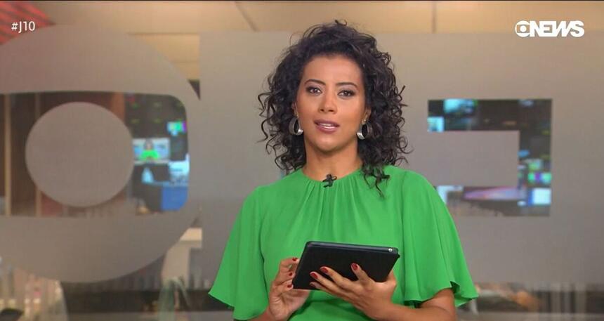 Aline Midlej de blusa verde e tablet na mão nos estúdios do Jornal da Dez