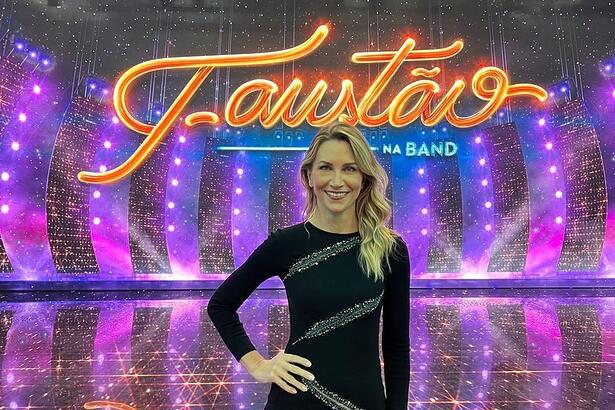 Anne Lottermann com um vestido preto, em frente ao telão nos estúdios do Faustão na Band, em uma foto posada