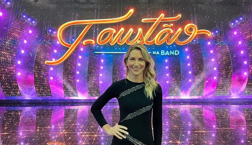 Anne Lottermann com um vestido preto, em frente ao telão nos estúdios do Faustão na Band, em uma foto posada