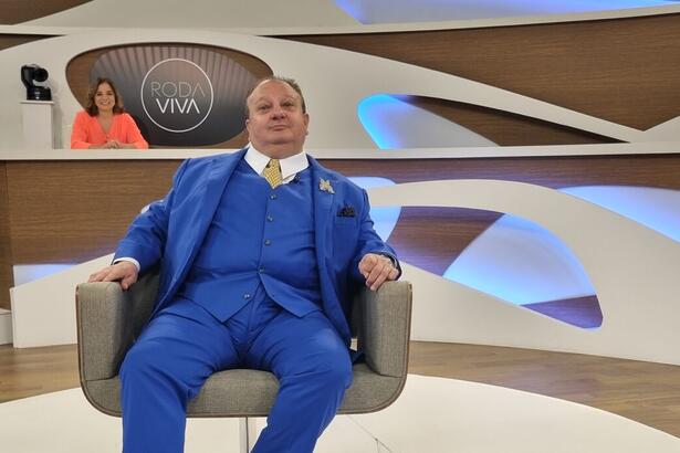 Erick Jacquin sentado na centro dos estúdios do programa Roda Viva. Ele veste um terno azul