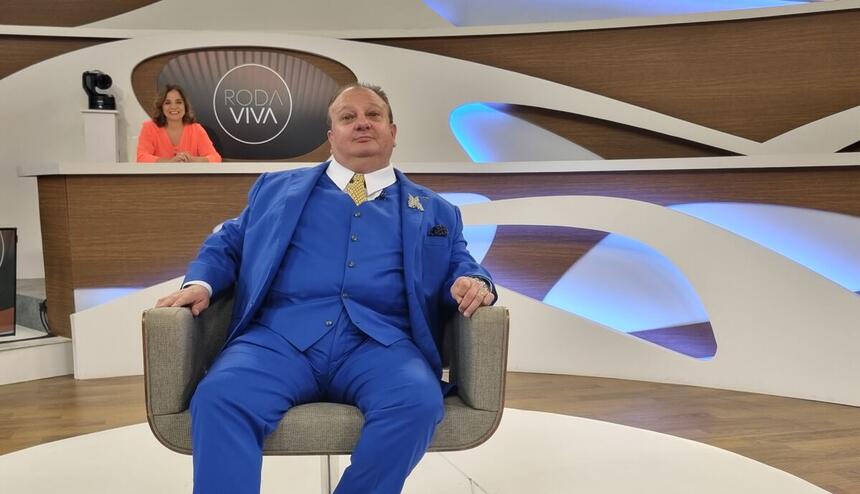 Erick Jacquin sentado na centro dos estúdios do programa Roda Viva. Ele veste um terno azul