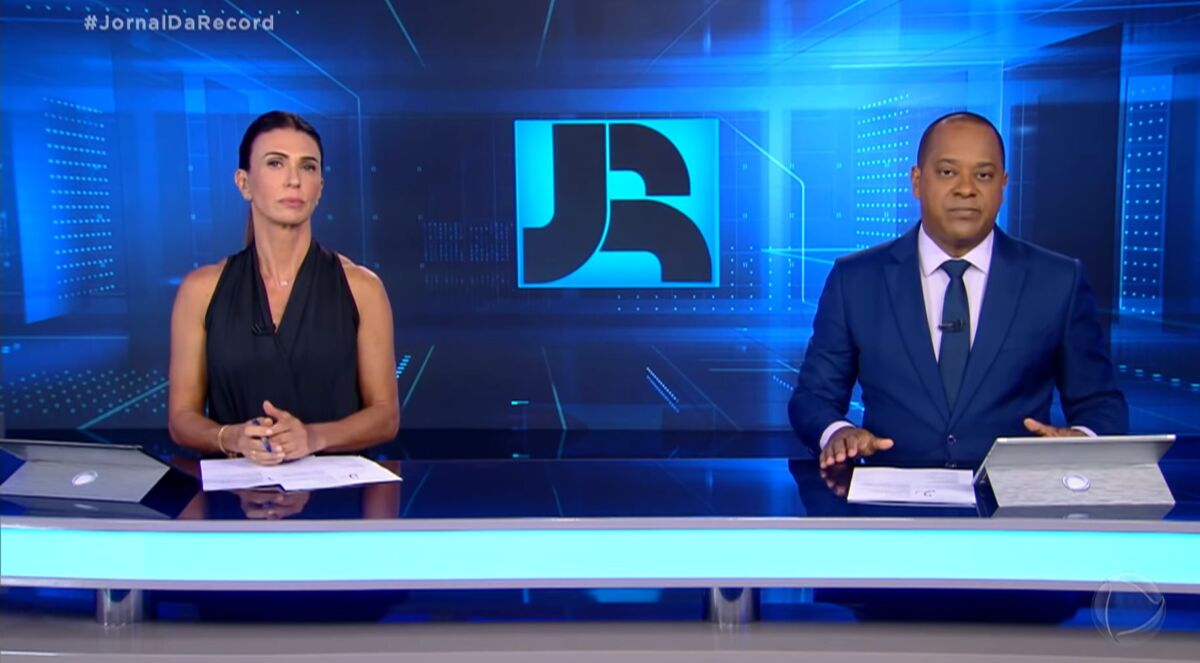 Janine Borba e Luiz Fara Monteiro sentados na bancada do Jornal da Record
