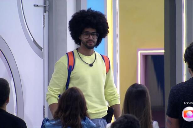 Luciano com a bolsa do BBB 22 nas costas em frente a porta de saída da casa