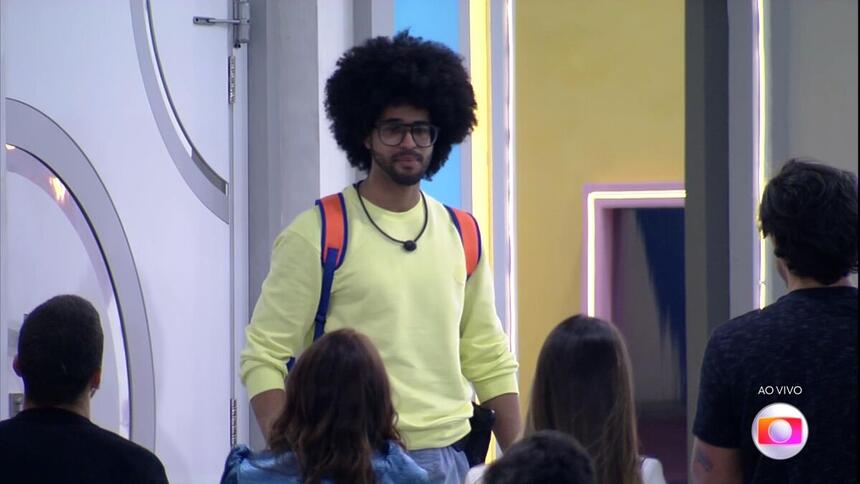 Luciano com a bolsa do BBB 22 nas costas em frente a porta de saída da casa