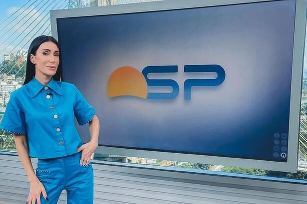 Michelle Barros de conjunto azul, em frente a televisão no estúdio do Bom Dia SP