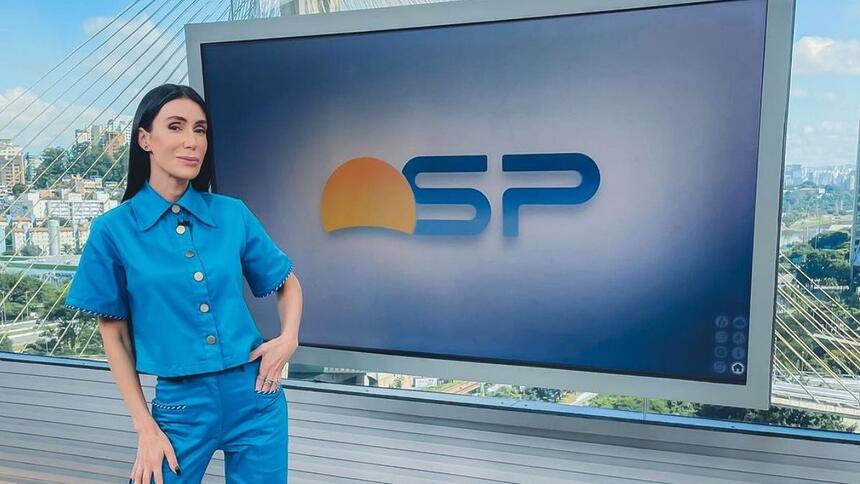 Michelle Barros de conjunto azul, em frente a televisão no estúdio do Bom Dia SP