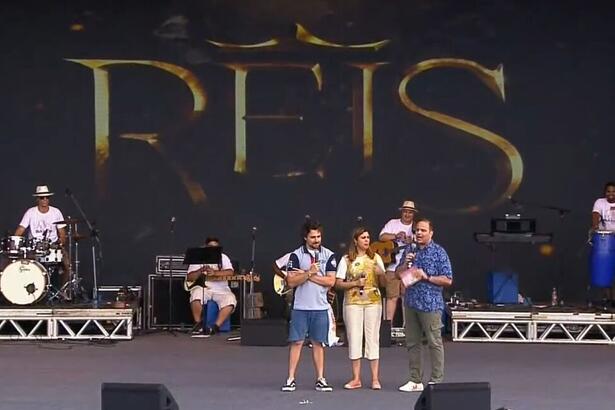 Miguel Coelho e Raphael Castro em cima de um palco, com o logo da novela Reis ao fundo