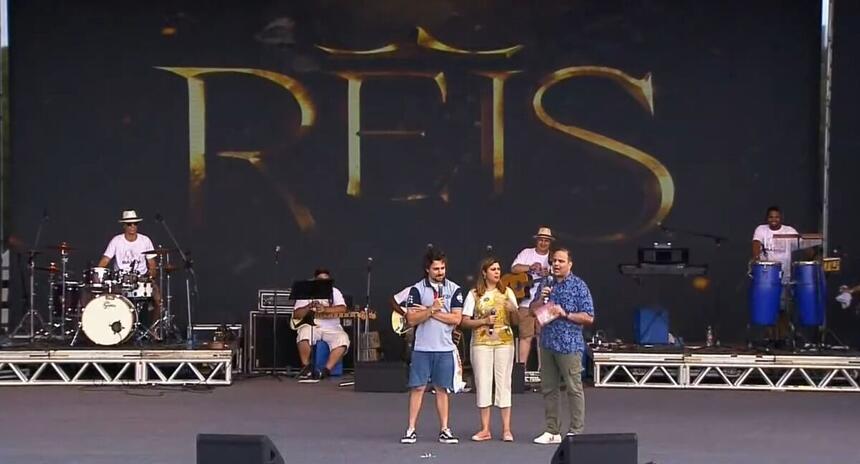 Miguel Coelho e Raphael Castro em cima de um palco, com o logo da novela Reis ao fundo