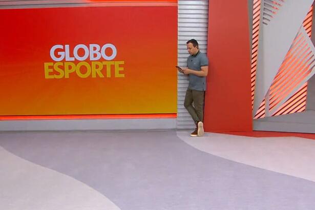 Tiago Medeiros mexendo no celular ao fundo dos estúdios do Globo Esporte PE