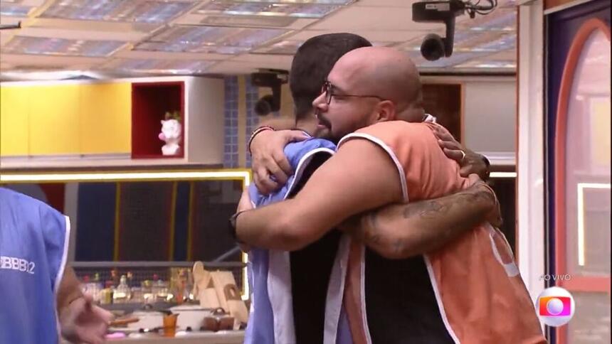 Tiago de colete laranja, abraça Pedro Scooby por ficar com a liderança, após venceram a prova no BBB 22.