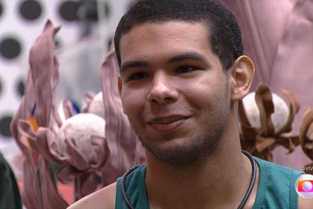 Vinicius sentado na sala do BBB 22 demonstra felicidade ao saber do resultado do primeiro jogo da discórdia do BBB 22