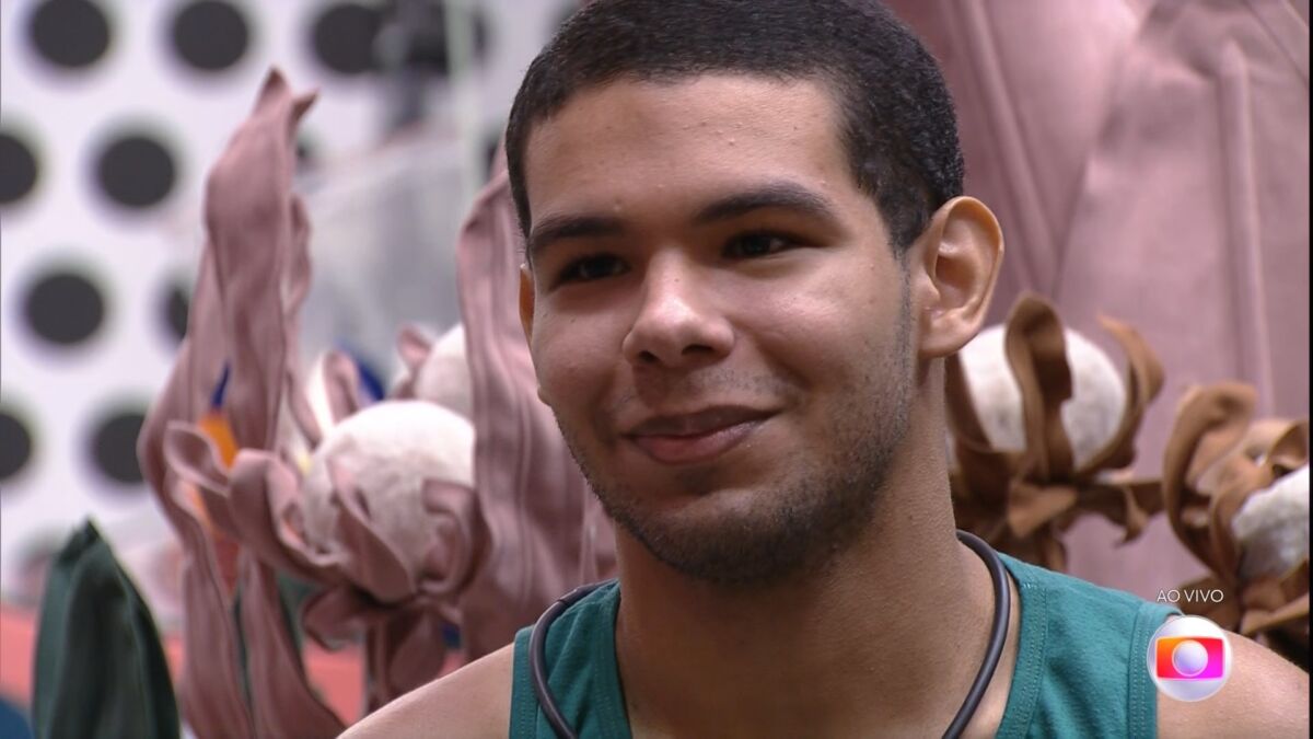 Vinicius sentado na sala do BBB 22 demonstra felicidade ao saber do resultado do primeiro jogo da discórdia do BBB 22
