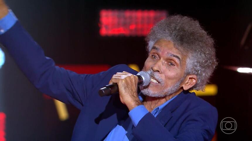 Arlindo Moita segura o microfone em apresentação no palco do The Voice+