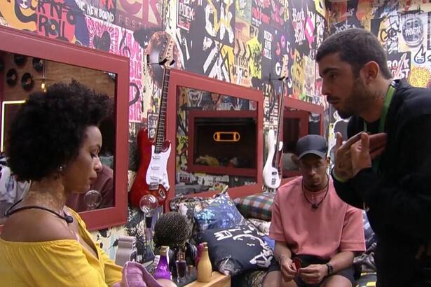 Natália sentada na cama, discute com Pedro Scooby que se encontra em pé no quarto grunge do BBB 22.