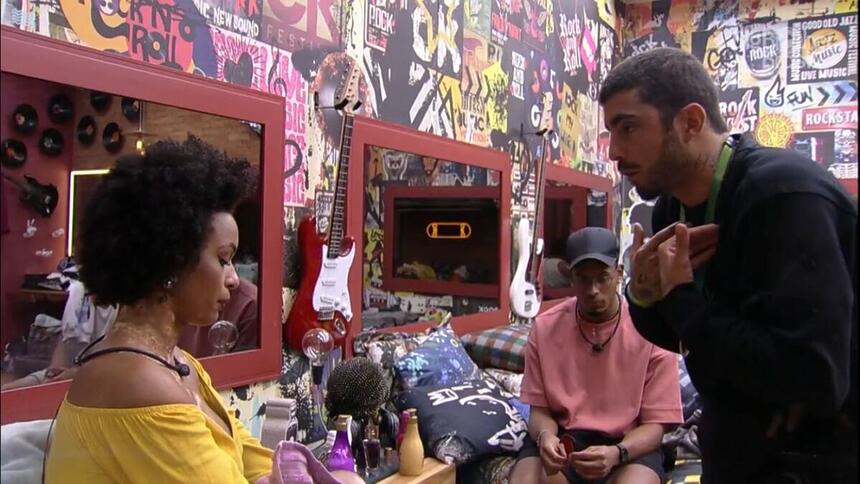 Natália sentada na cama, discute com Pedro Scooby que se encontra em pé no quarto grunge do BBB 22.