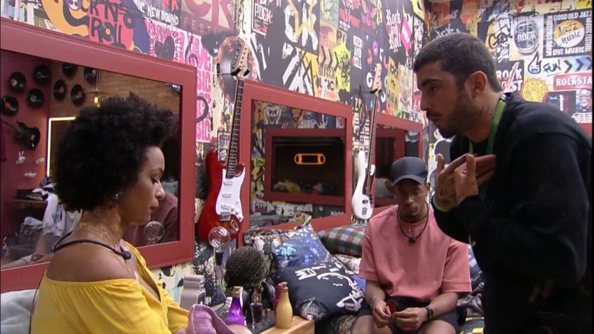 Natália sentada na cama, discute com Pedro Scooby que se encontra em pé no quarto grunge do BBB 22.