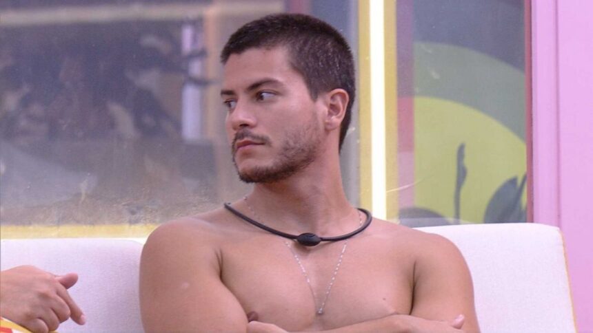 Arthur Aguiar sem camisa, olhando para o lado, sentado na varanda do BBB 22