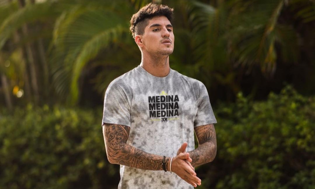 Gabriel Medina em uma foto na praia, utilizando uma camiseta branca estampada com sua marca