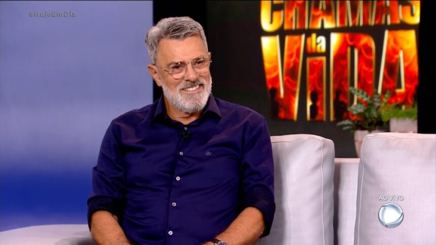 Raymundo de Souza sentado no sofá do programa Hoje em Dia. Por trás está um telão com o logo da novela Chamas da Vida que o ator foi divulgar