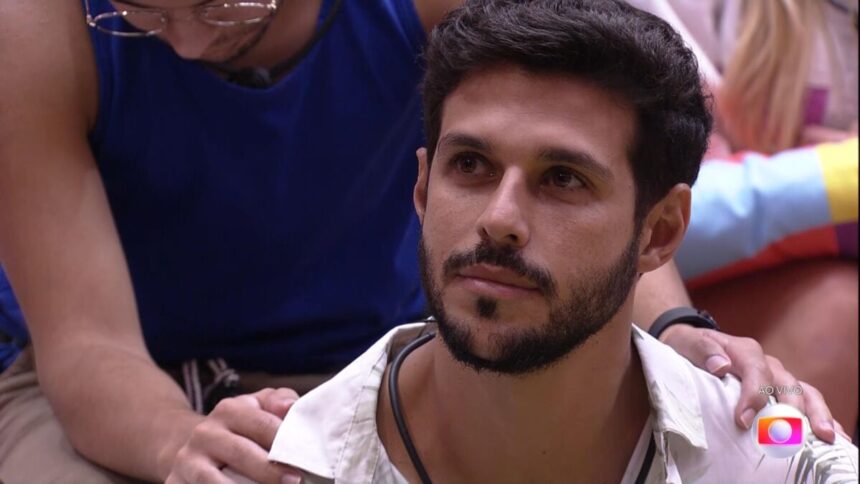 Sentado no chão da sala, Rodrigo escuta discurso de Tadeu Schmidt antes de ser eliminado no BBB 22