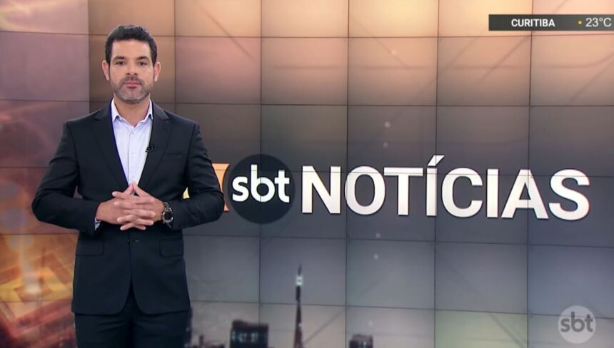 Darlisson Dutra nos estúdios do SBT Notícias, em frente ao telão do noticiário